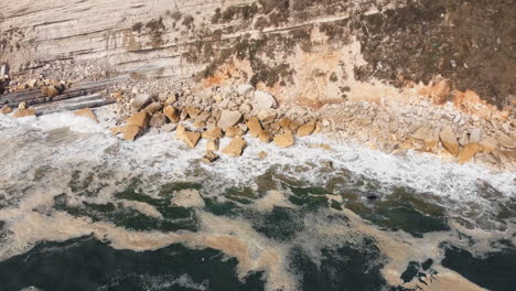 Aerial-tilt-up-shot-showing-green-Atlantic-ocean-with-waves-and-orange-colored-cliffs-in-Portugal-lighting-by-sun