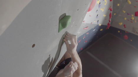 High-Angle-Shot-Of-Young-Man-Climbing-Up-Artificial-Rock-Wall-And-Gripping-At-Handholds