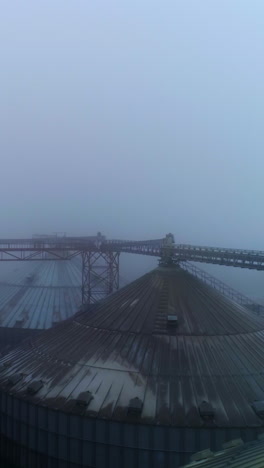 metal supports connecting the tops of huge silo tanks. powerful granary reservoirs in foggy winter weather. top view. vertical video