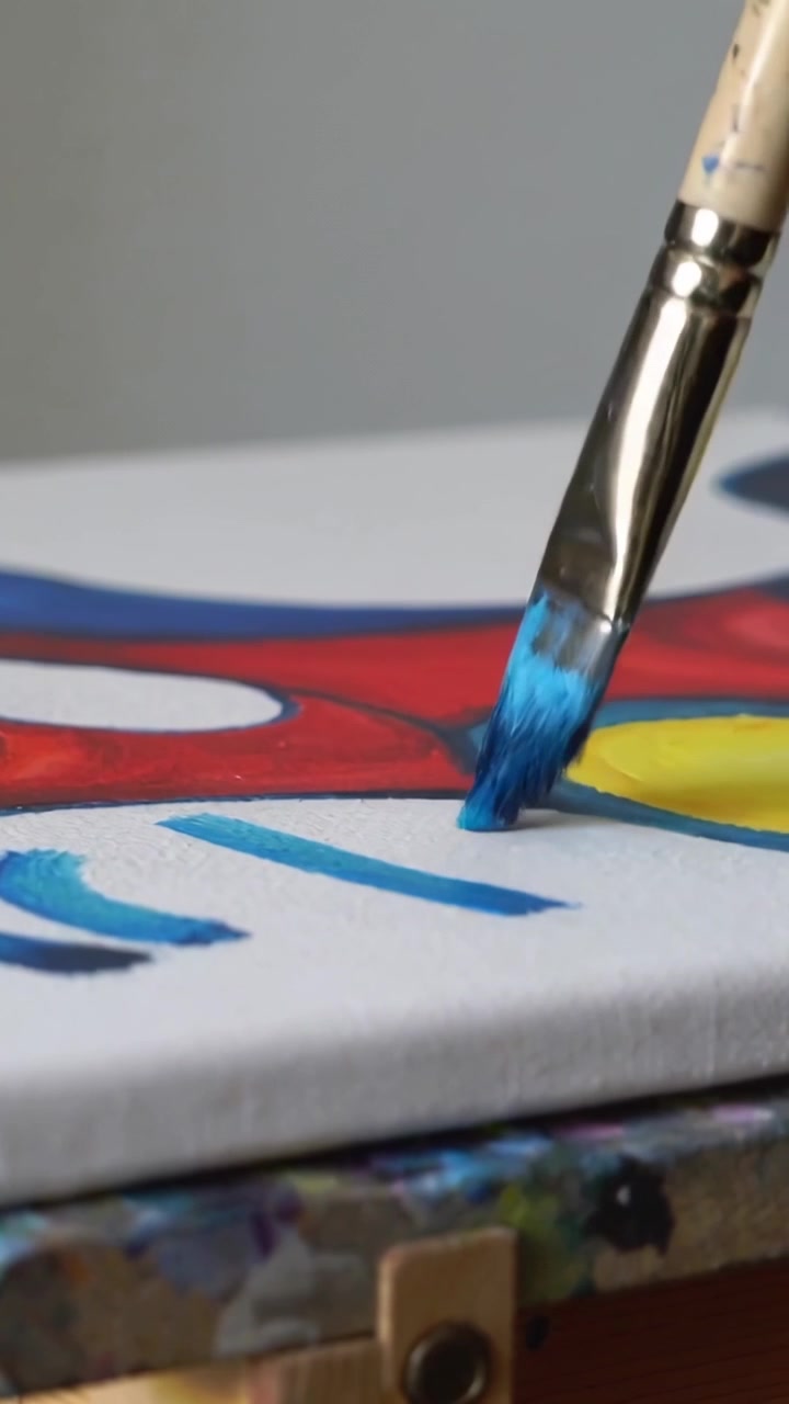 Vídeo vertical: Pincel de pintura tocando linha vermelha, desenhando espiral azul em cavalete, acentuando disco amarelo.