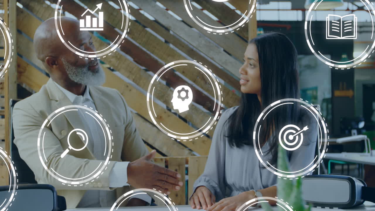 Animation of digital icons against diverse businessman and businesswoman shaking hands at office