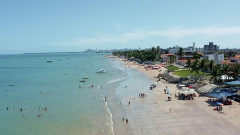 aerial drone shot of the tropical bessa beach in the coastal capital city of joao pessoa, paraiba, brazil with people enjoying the ocean and fishing boats at shore on a warm sunny summer day