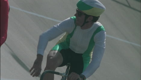 two men ride bicycles one waves and makes a hand gesture