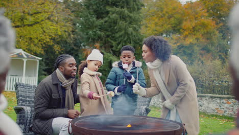 Familia-Multigeneracional-Tostando-Y-Comiendo-Malvaviscos-Parados-Alrededor-De-Una-Hoguera-O-Barbacoa-En-El-Jardín-De-Casa---Filmados-En-Cámara-Lenta