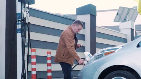 refueling process of an electric car. a shot under the hatch where the electric eco car charges. the electric car charging hatch opens automatically. a male hand inserts an erectile car