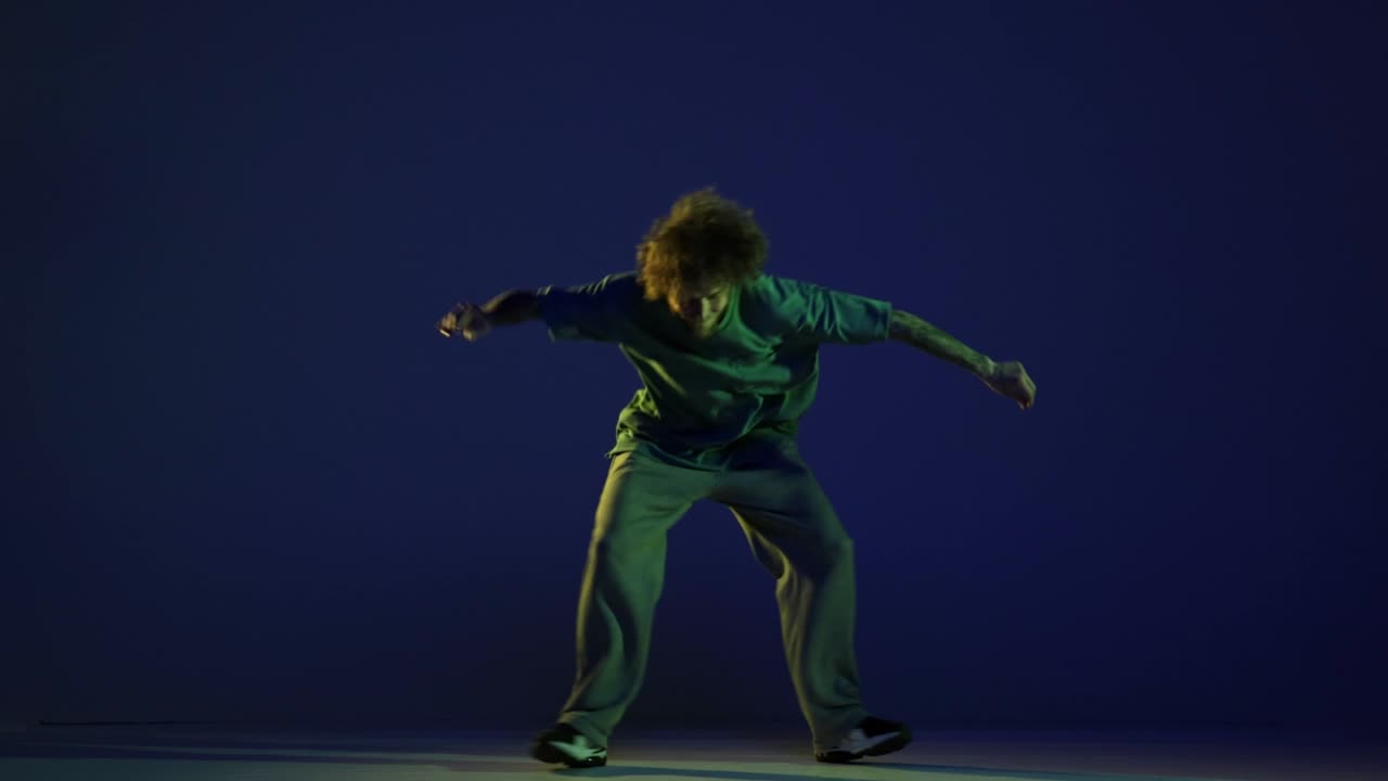 Stylish young man, hip-hop dancer dancing isolated over dark blue background in neon light. Modern dance art, fashion, youth, ad, style. 4K, video