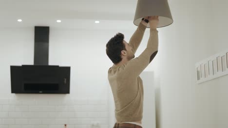 White-man-unscrewing-light-bulb-at-open-kitchen.-Guy-standing-under-chandelier