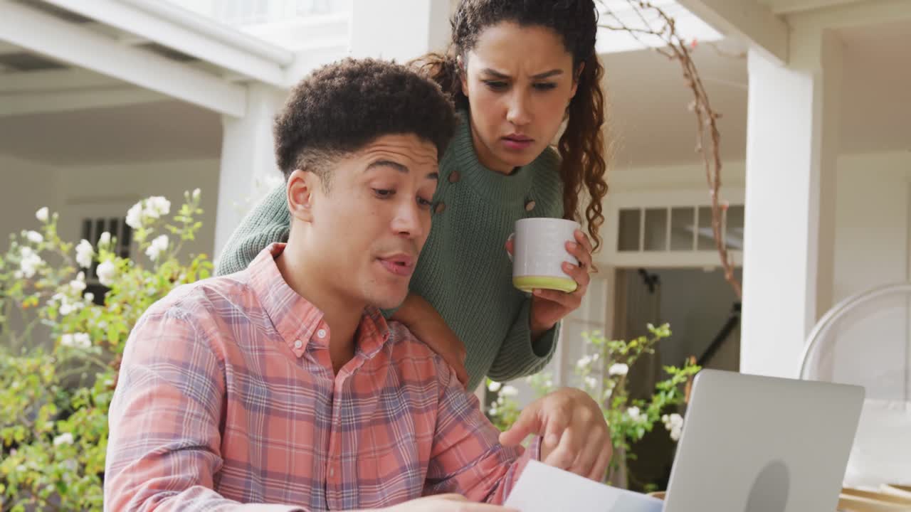 video de una pareja biracial usando una computadora portátil en el jardín