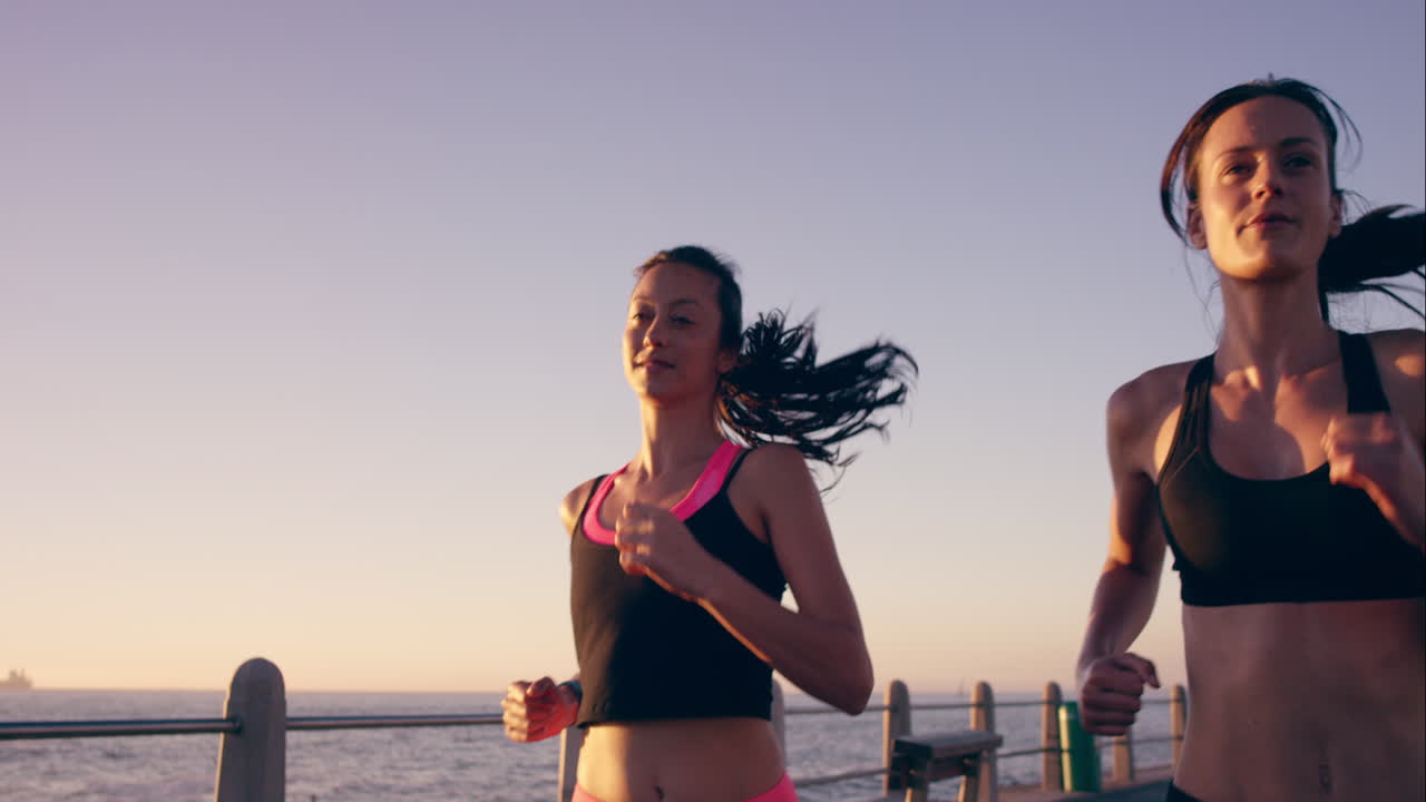 Two athletic woman running outdoors slow motion on promenade at sunset near ocean enjoying evening run