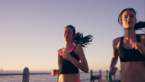 dos mujeres atléticas corriendo al aire libre en cámara lenta en el paseo marítimo al atardecer cerca del océano disfrutando de la carrera nocturna