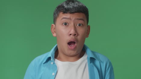 The Portrait Of A Young Asian Boy Opening Her Eyes With Palms , Surprised And Saying Wow In The Green Screen Studio