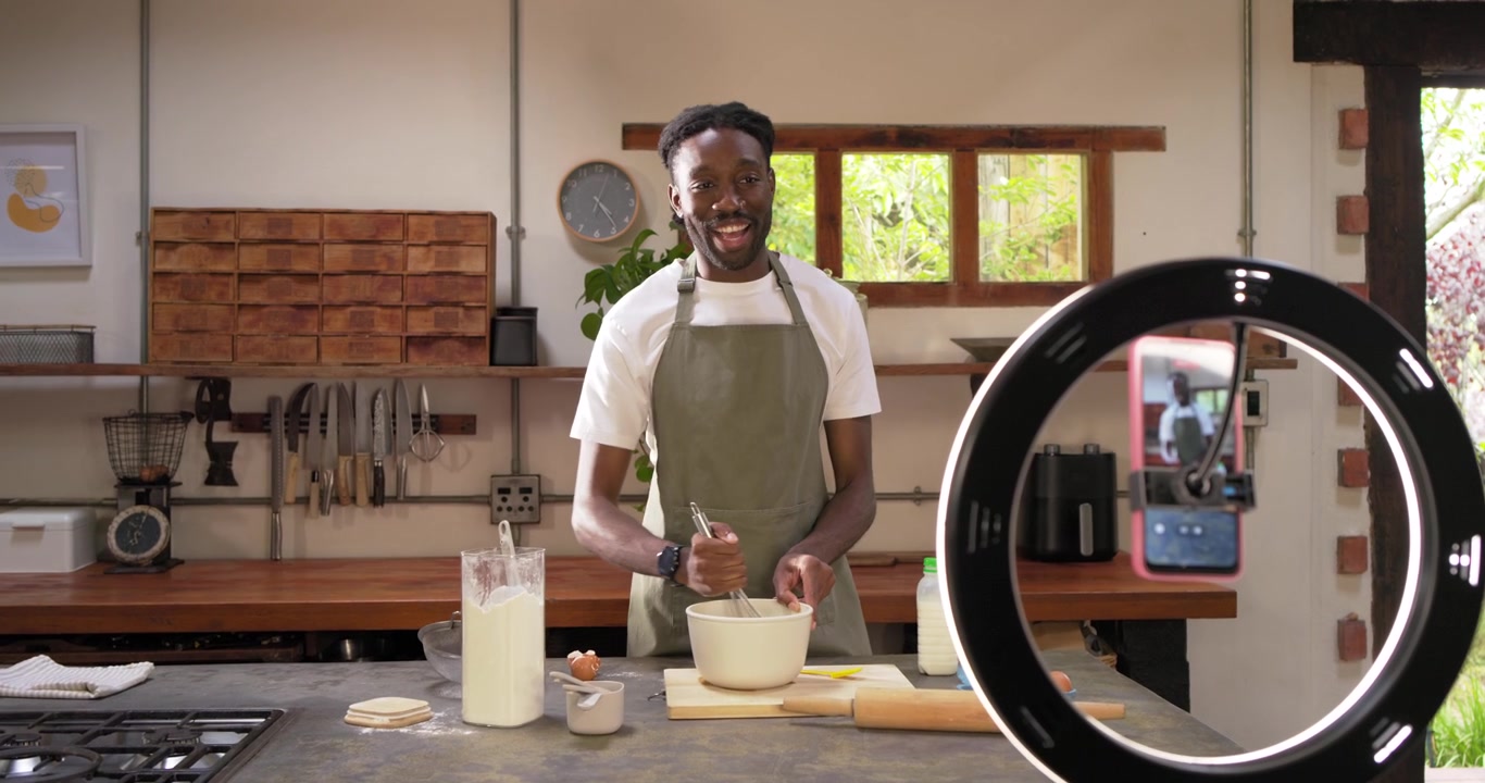 Registrazione con telefono: un uomo afroamericano con grembiule mescola in una ciotola sul bancone della cucina, mostrando una ricetta.