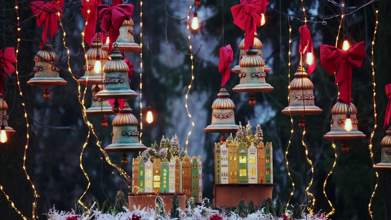 Close up of festive Christmas decorations with hanging bells, red bows, and warm glowing lights in a winter park setting