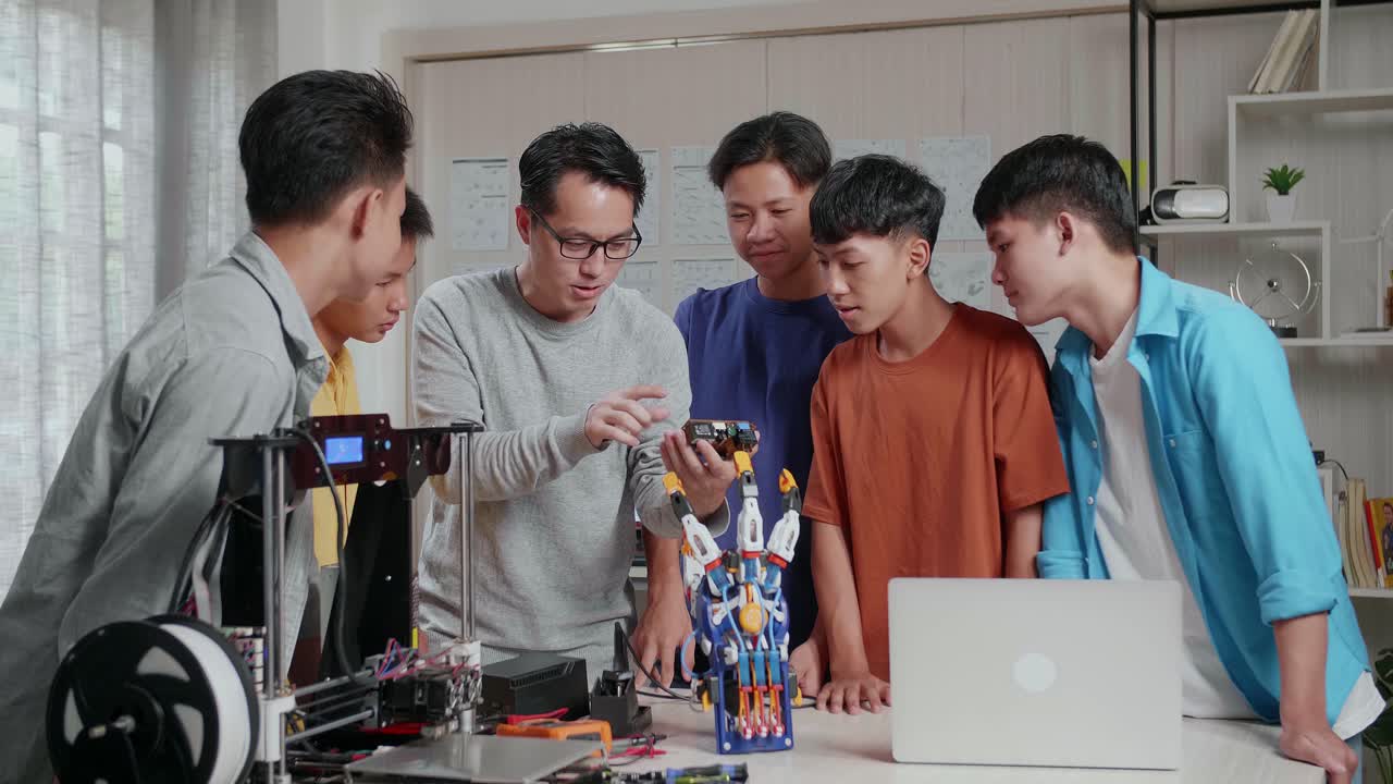 노트북, 3d 프린팅, 사이보그 손을 가진 아시아 남자가 학교의 소년들에게 회로판에 대해 설명합니다.