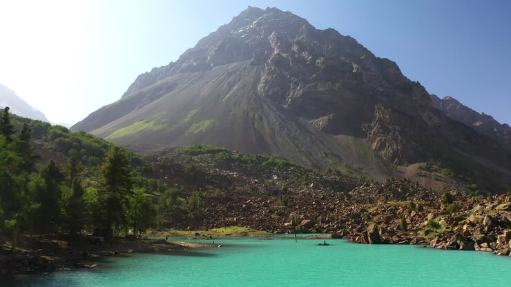 Drone shot of man swimming in turquoise colored water in the mountains at Naltar Valley in Pakistan, aerial shot