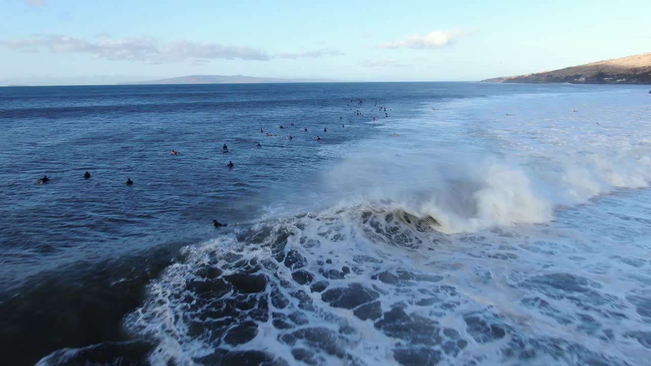 flying out over lots of surfers sitting and waiting for waves during record swell on maui hawaii