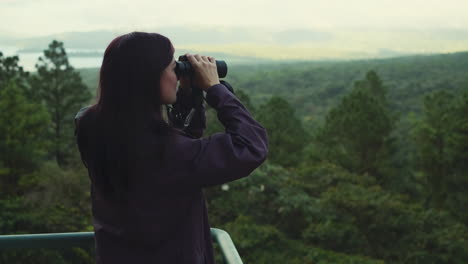 Handheld-shot-of-young-woman-looking-through-binoculars-in-green-forest