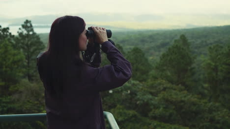 handheld shot of young woman looking through binoculars in green forest