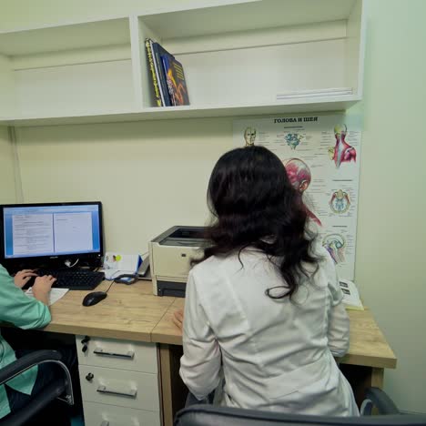 patient leaves the doctor's room. female specialist works in a modern clinic. assistant writes the results of patient's examination on the computer. healthcare concept.
