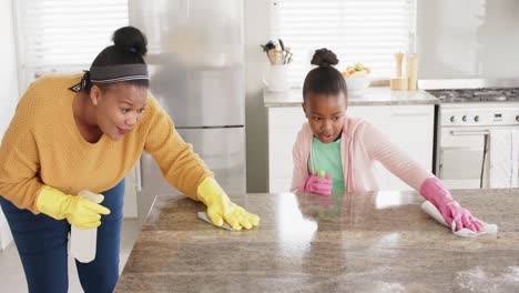 happy african american mother and daughter cleaning countertop in kitchen, slow motion