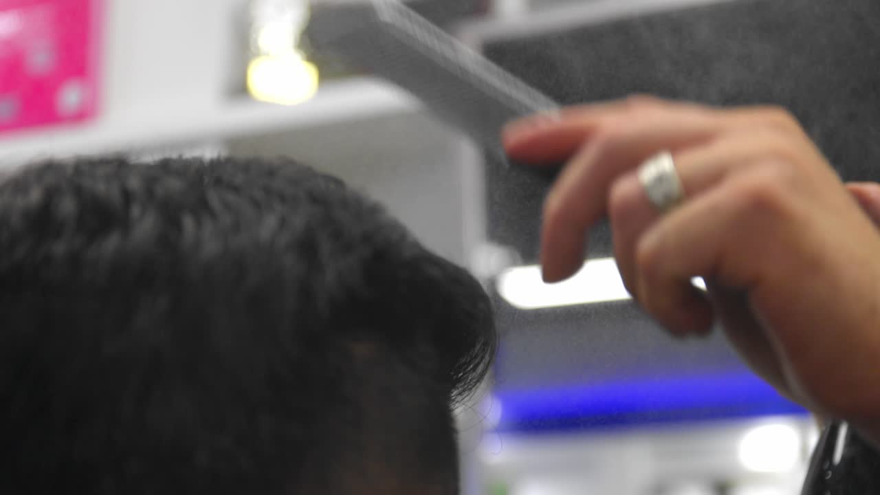 peluquero peinando el cabello de los hombres mientras moja el cabello con una botella de spray negra llena de agua