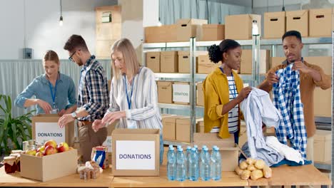 multiethnic group of volunteers packing boxes with food and clothes in charity warehouse