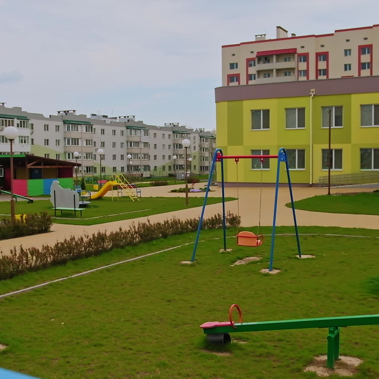 Pleasant good-looking territory of new kindergarten. Adorable playgrounds with teeterboards on the green grass. New residential area backdrop
