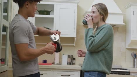 una pareja feliz y diversa sonriendo y bebiendo café en casa.