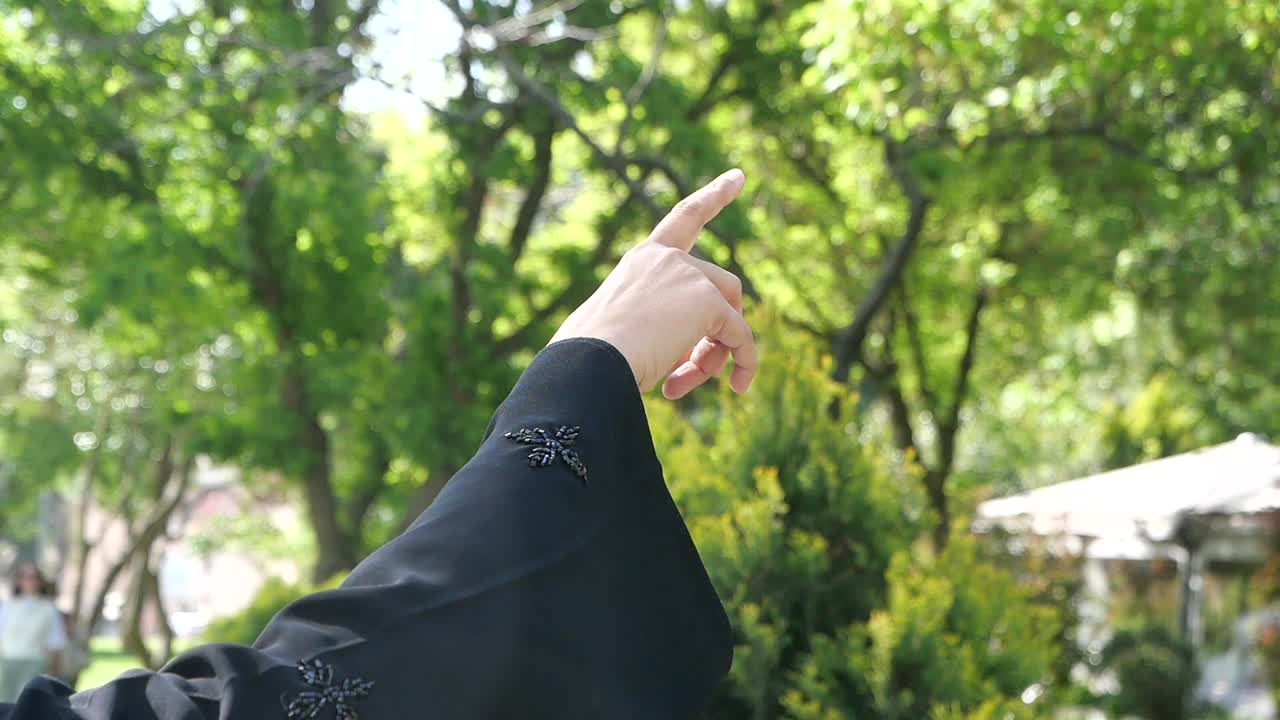 Woman in abaya pointing at trees in a park