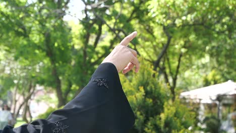 woman in abaya pointing at trees in a park