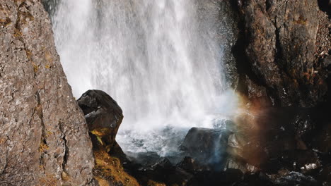 rainbow-colored mist rises out of pool at base of iceland waterfall