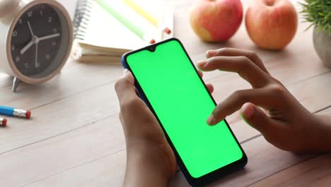child using a smartphone with green screen display at a desk