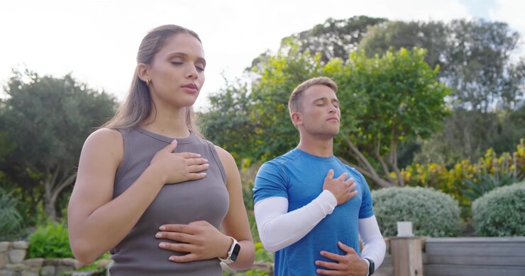 Fitnesskoppel in sportkleding volgt aanwijzing, handen op borst en buik, ademt in tuin, smartwatch