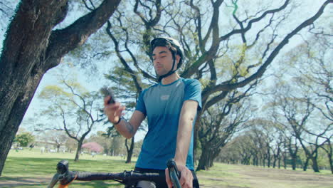 cyclist standing with bike in the park and using smartphone
