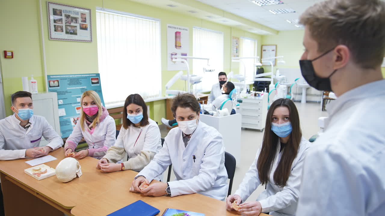 Dentistry class in university auditory. Students are sitting together at the desk, holding models of teeth in hands and listening to one student speaking.
