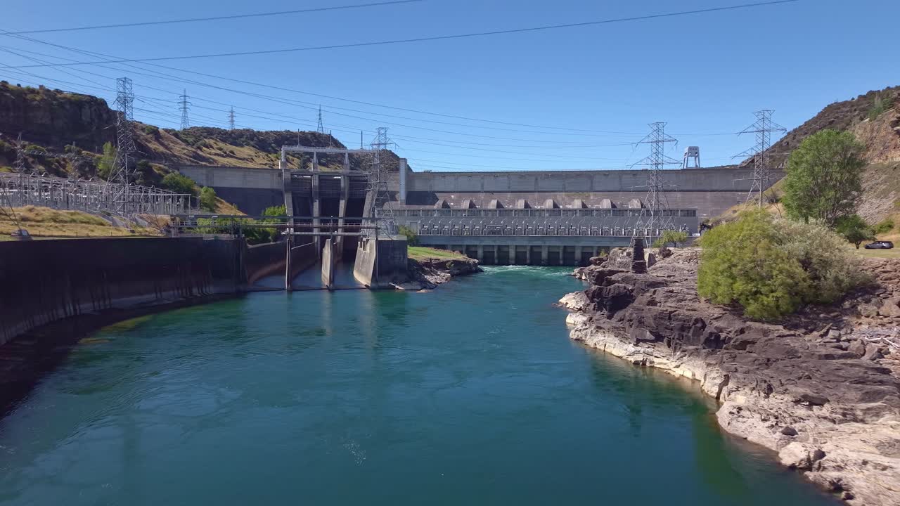 Aerial drone shot flying in reverse low over the Clutha River, revealing the full span of Roxburgh hydroelectric dam in Central Otago, New Zealand