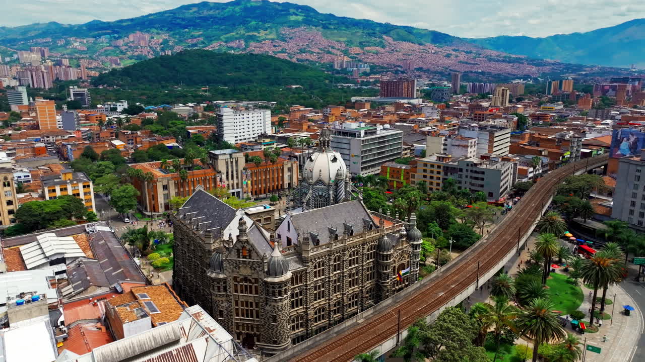 Imagem de drone do Metrô de Medellín perto da Praça Botero, em Medellín, Colômbia, capturando o transporte urbano, a arquitetura da cidade e o movimento dos trens pela paisagem do centro.