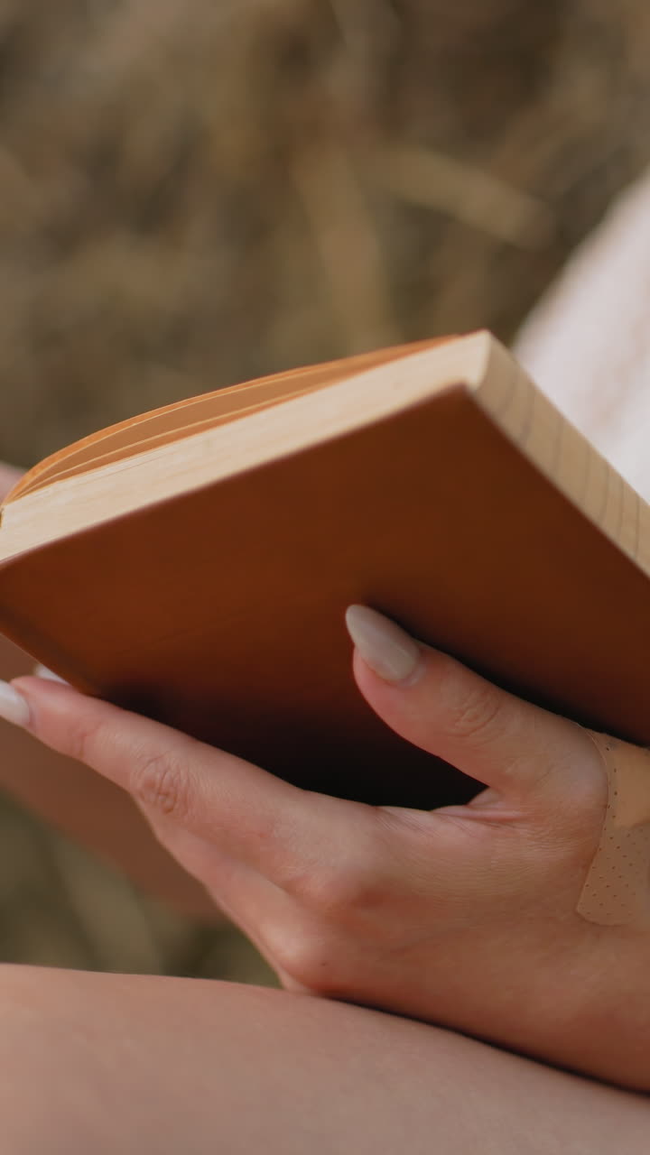 primer plano de una mujer con un libro abierto, los dedos girando suavemente la página, mientras lee con atención, el fondo suave y borroso mejora el entorno pacífico del campo