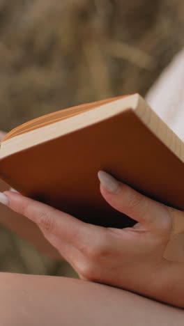 primer plano de una mujer con un libro abierto, los dedos girando suavemente la página, mientras lee con atención, el fondo suave y borroso mejora el entorno pacífico del campo