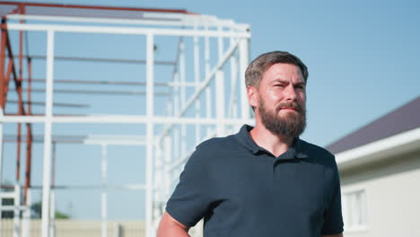 bearded man in dark polo near metal frame structure folds pneumatic rifle, break barrel action with careful safety check, focused squint under bright summer daylight, rural yard setting