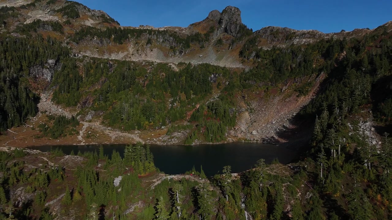 Ripresa cinematografica 4K con drone che si espande verso l'esterno da un incontaminato lago alpino in cima al 5040 Peak, BC. Circondato da montagne aspre e foreste di pini. Ideale per progetti su natura, avventura e viaggi