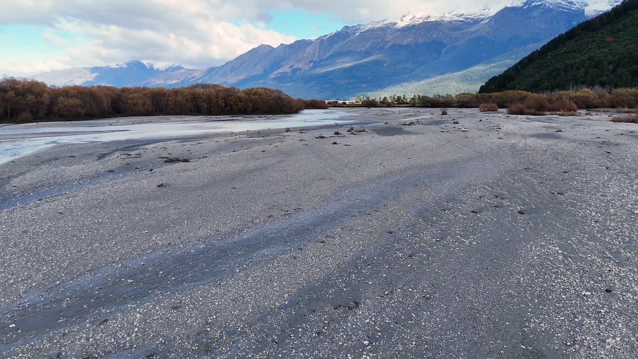 Camera slowly pans across gravel bar and stream, revealing mountains under soft natural daylight