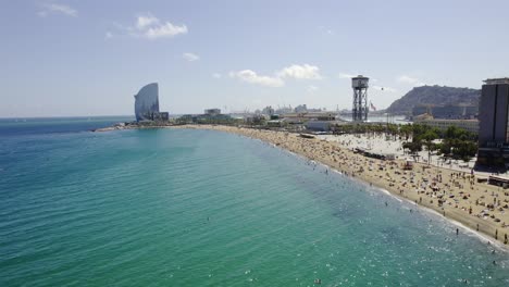 aerial view of a bustling beach in barcelona, featuring the w hotel and cable car