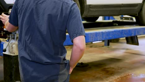 Un-Técnico-De-Servicio-Automotriz-Visto-Levantando-Un-Vehículo-En-Un-Polipasto-En-Preparación-Para-Trabajar-En-él.