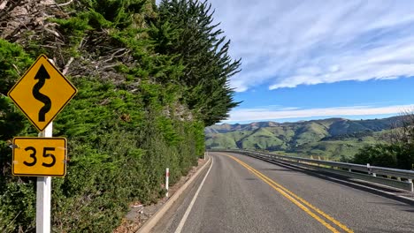 an ambulance travels through a winding road in akaroa, new zealand, under clear skies and lush greenery