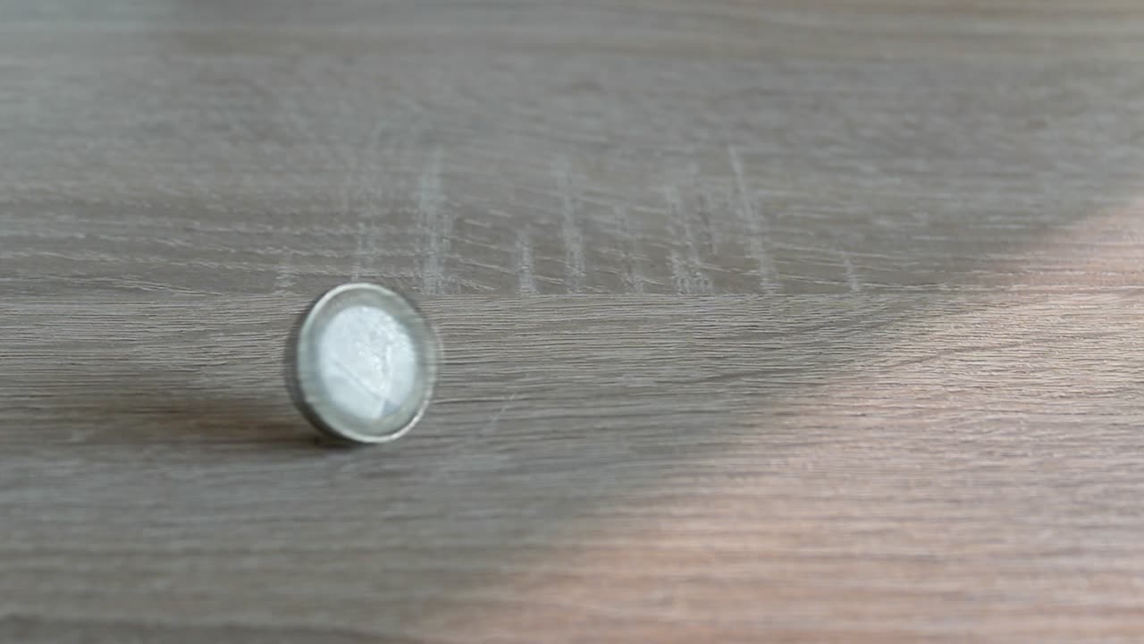 una moneda de euro gira sobre una mesa interior de madera y luego cae sobre su parte trasera
