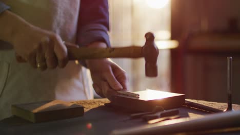 close up of hands of caucasian female jeweller using hammer, making jewelry