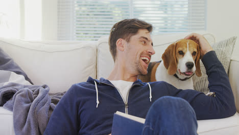 Smiling-man-sitting-on-ground-stroking-his-pet-while-reading-book-4K-4k