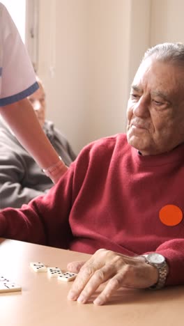 nurse playing dominoes with senior man and woman in canteen of nursing home