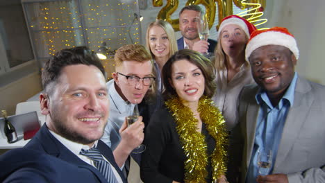 businessman holding camera and taking selfie with happy colleagues at new years party in office